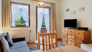 A room with a sofa, a dining table, a wooden cabinet with a television, and a window with curtains. - Apartment '3 Kapelle' with Mountain View, Shared Terrace and Wi-Fi (Todtnau)