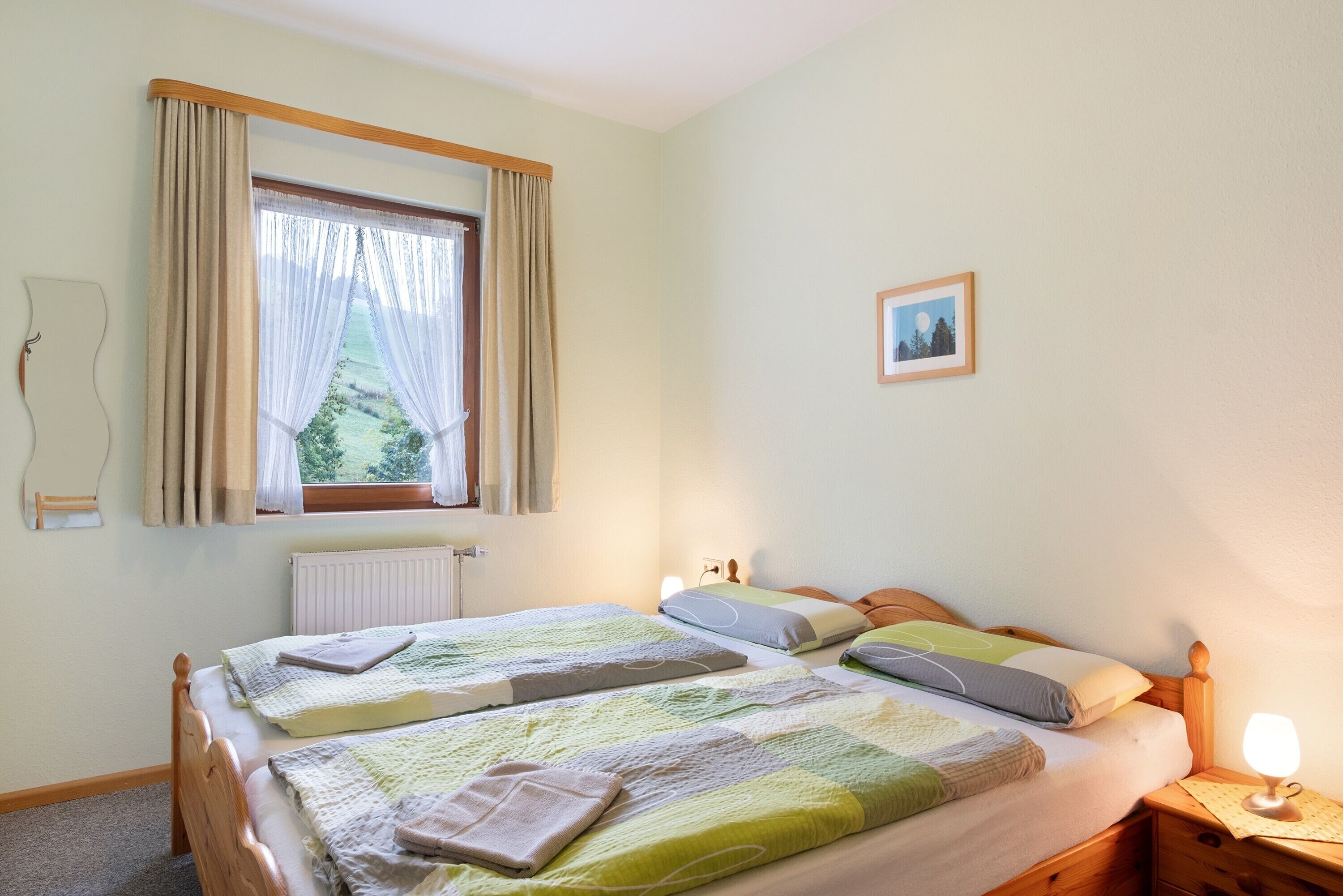A bedroom with two beds, a window with curtains, a bedside lamp, and a framed picture on the wall.