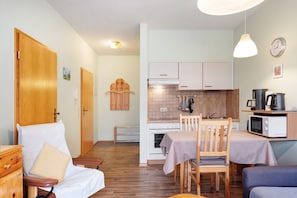 A compact living space with a kitchenette, a dining area, and a seating area with a chair and a sofa. - Apartment '3 Kapelle' with Mountain View, Shared Terrace and Wi-Fi (Todtnau)