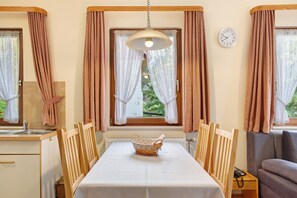 Ein Zimmer mit Esstisch, Stühlen, einem Korb, einer Couch, einem Fenster mit Vorhängen, einer Uhr und einem Heizkörper.