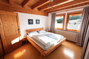 A wooden-framed bedroom with a bed, a nightstand, a window with curtains, and a view of a snowy landscape.