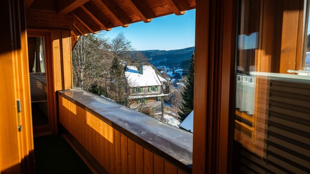 A wooden balcony with a view of a house and trees. - Apartment 'Monika' with Mountain View, Balcony and Wi-Fi (Schonach im Schwarzwald)