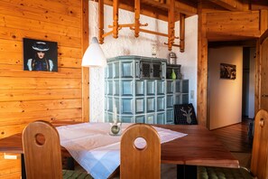 A wooden interior with a dining table, chairs, a cabinet, and a wall-mounted lamp.