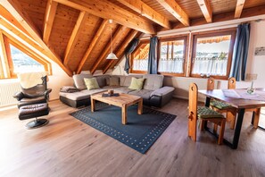 A cozy living room with a wooden ceiling, a sofa, a coffee table, and a dining table with chairs.