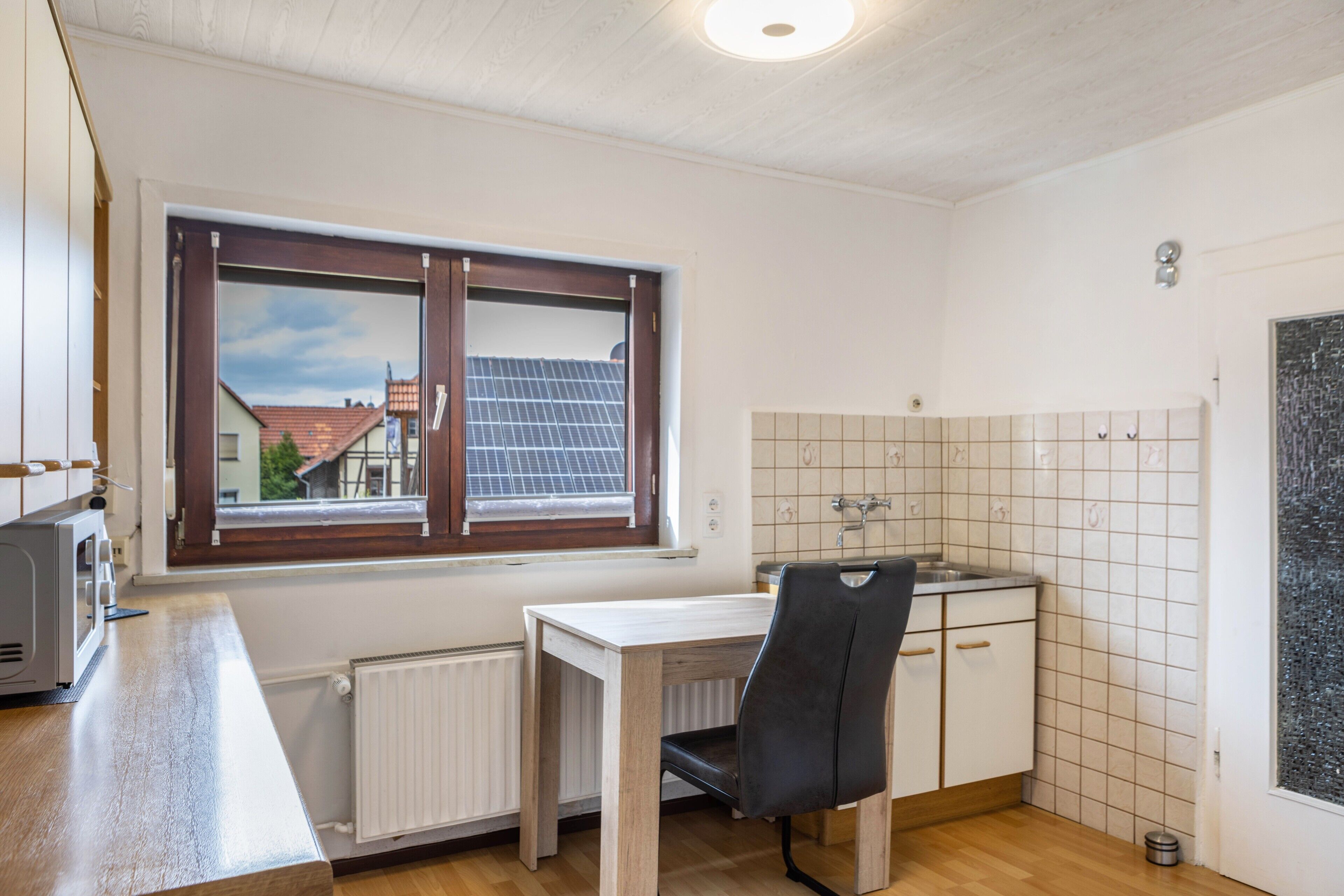 Een keuken met een raam, een tafel, een stoel, een radiator en een betegelde achterwand.