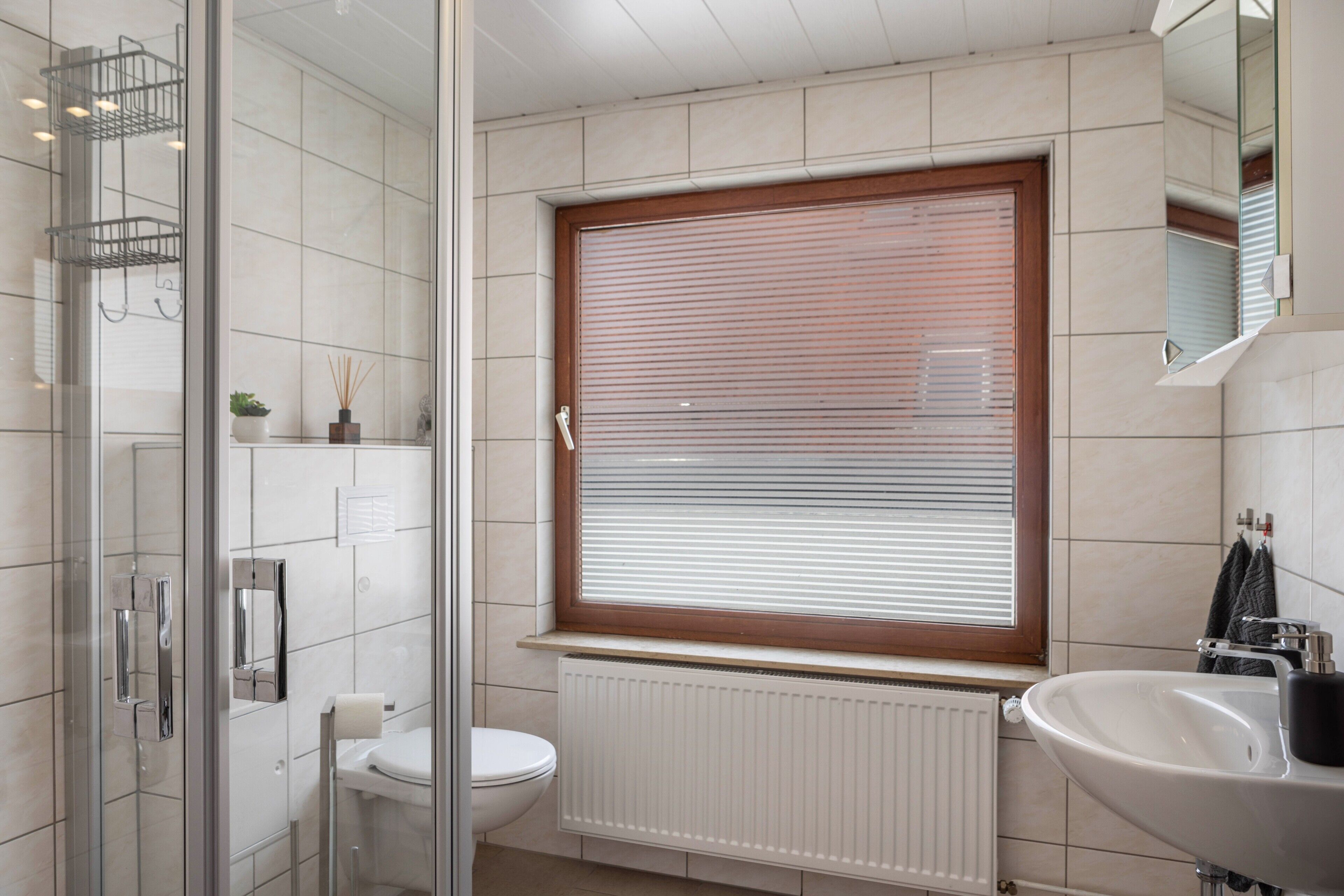 A bathroom with a toilet, a sink, a window with blinds, a shower area, and a radiator.