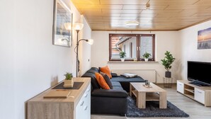 Una sala de estar moderna con un sofá modular, una mesa de centro, un televisor y una ventana con plantas.