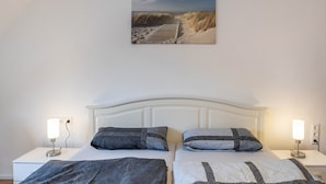 Habitación de hotel con dos camas, cabecero blanco, lámparas de noche y un cuadro con una escena de playa en la pared.