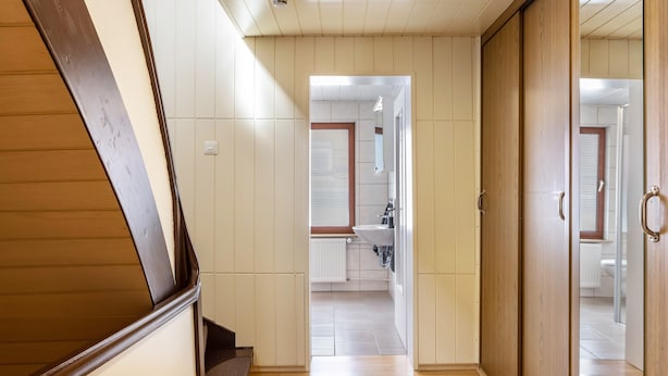 Pasillo que conduce a un baño con lavamanos e inodoro, suelo de madera y puerta con pomo circular.