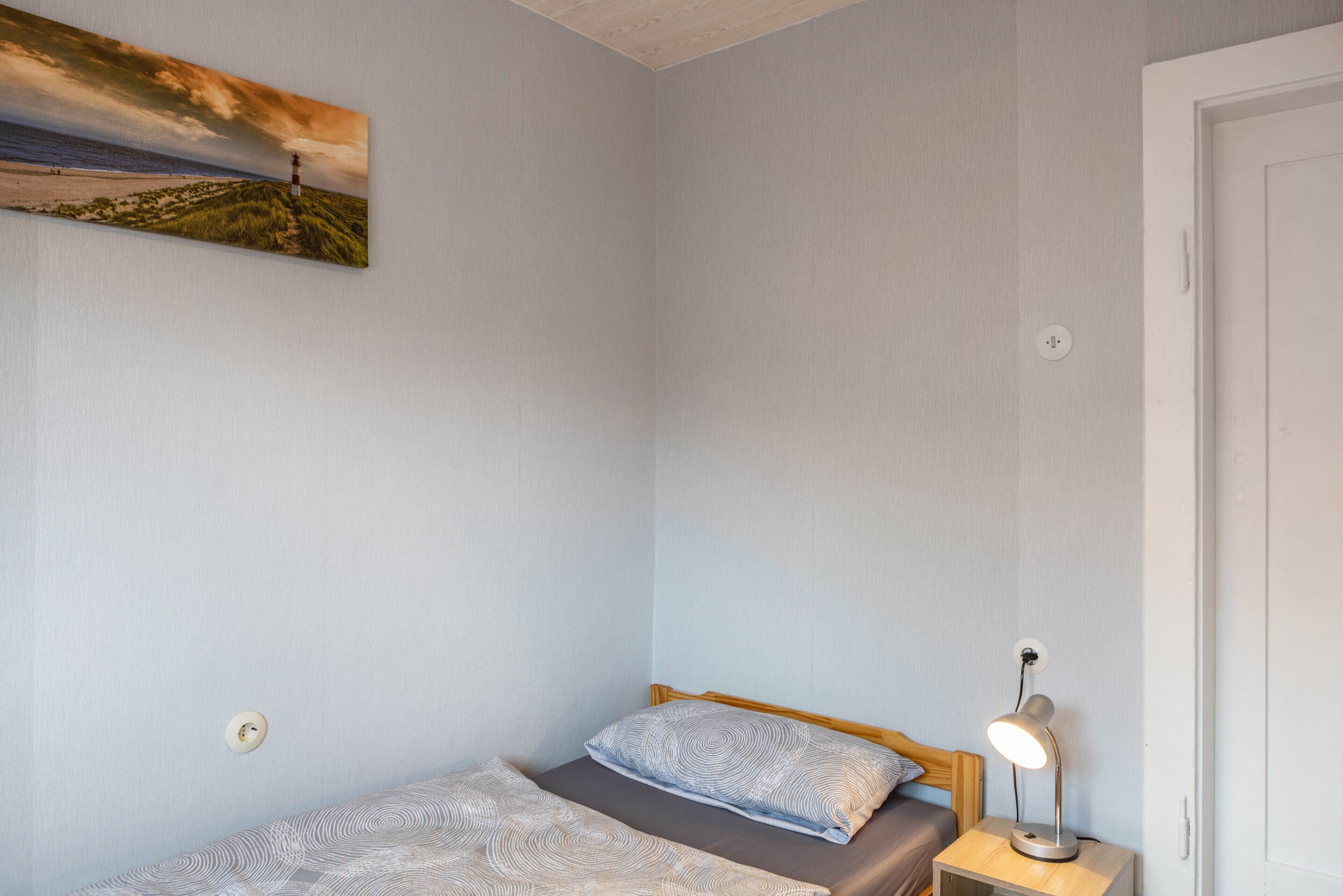 Una camera da letto con un letto, una lampada da comodino, un quadro appeso al muro e una porta.