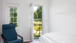 A room with a bed, a chair, a window, and a door leading to a garden. - Apartment 'Schloss Glücksburg' with Lake View, Private Garden and Wi-Fi (Glücksburg (Ostsee))