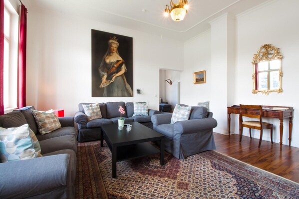 A living room with sofas, a coffee table, a rug, a painting, a chandelier, and a wooden desk. - Apartment 'Schloss Glücksburg' with Lake View and Wi-Fi (Glücksburg (Ostsee))