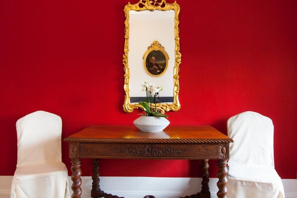 Una habitación con una pared roja, una mesa de madera con un jarrón blanco y dos sillas blancas.