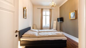 A bedroom with a bed, a chandelier, a television, and a window with curtains. - Apartment 'Schloss Glücksburg' with Lake View and Wi-Fi (Glücksburg (Ostsee))