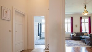A hallway leading to a living area with a sofa set, a chandelier, and a framed certificate on the wall. - Apartment 'Schloss Glücksburg' with Lake View and Wi-Fi (Glücksburg (Ostsee))