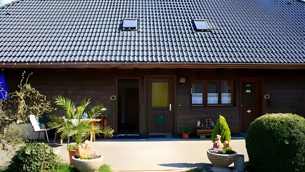 Un bâtiment avec un toit recouvert de tuiles, une porte d’entrée et des plantes en pot.