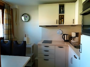 Een kleine keuken met een eettafel, stoelen, een klok en essentiële apparaten.