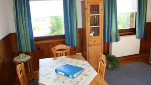 Une pièce avec une table en bois, des chaises, un buffet et une fenêtre avec des rideaux.
