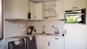 Une cuisine compacte avec des meubles blancs, une machine à café, un évier et une fenêtre donnant sur un paysage verdoyant.