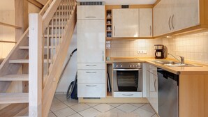 A kitchen with wooden cabinets, a built-in oven, a dishwasher, and a staircase.