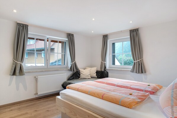 A bedroom with two windows, a bed, a radiator, and a wooden floor.