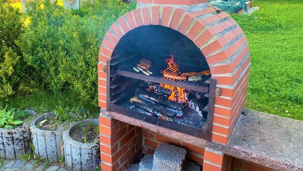 A brick outdoor grill with food being cooked.