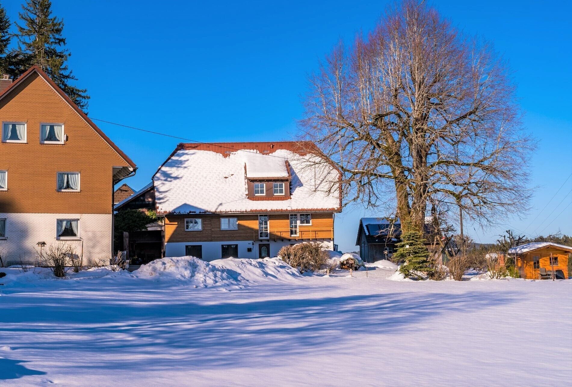 A two-story house with a snow-covered roof and a clear blue sky.