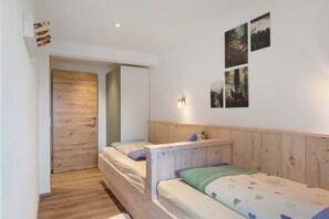 Een slaapkamer met twee houten bedden, een houten hoofdbord, een wandlamp en een deur naar een andere kamer.