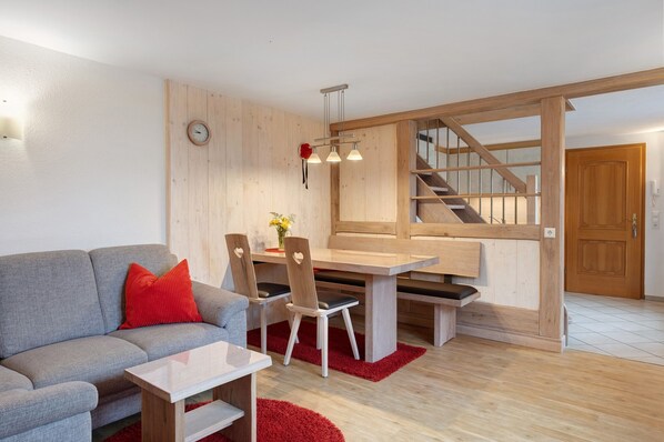 Een moderne woonkamer met een grijze bank, een houten eettafel en een trap.