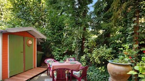 Un jardín con una mesa, sillas, un cobertizo y una maceta grande.