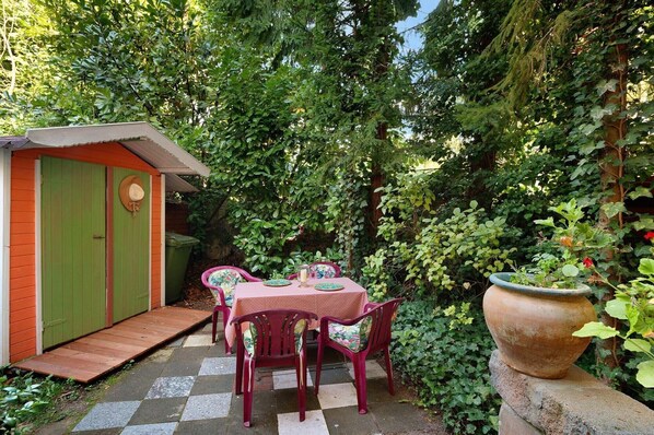 A garden with a table and chairs, a shed, and a large planter.