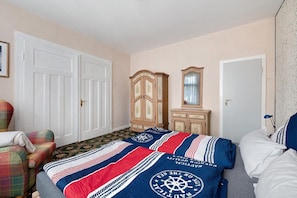 A bedroom with a bed, a chair, a wardrobe, and a mirror.