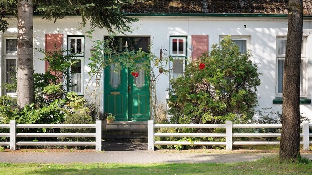 Un edificio con puerta verde, paredes blancas y una cerca blanca al frente.