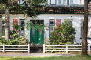 Un bâtiment avec une porte verte, des murs blancs et une clôture blanche devant.