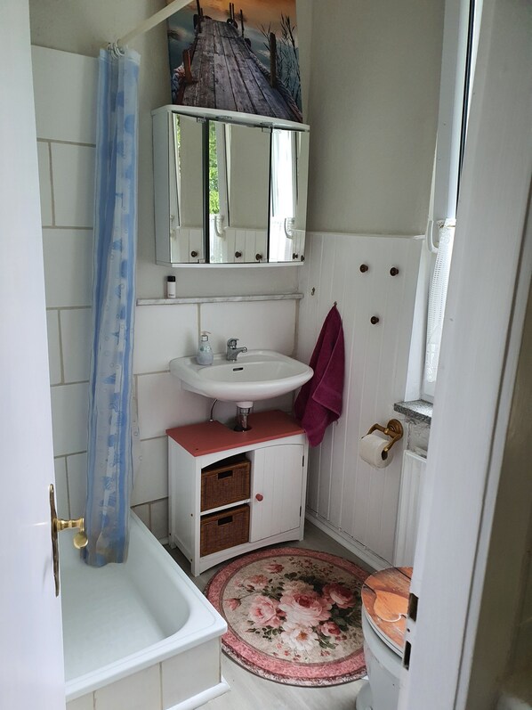 Une salle de bain avec un lavabo blanc, un miroir au-dessus, un rideau de douche, un tapis rond et des toilettes.
