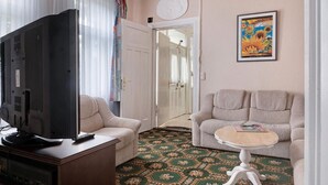 Una habitación con una televisión sobre un mueble de madera, dos sofás, una mesita redonda y una alfombra estampada.