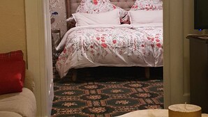 Un dormitorio con cama, papel tapiz floral, un cuadro en la pared y alfombra estampada.