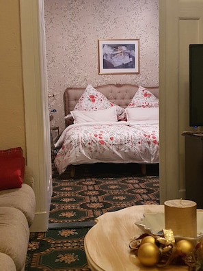 A bedroom with a bed, floral wallpaper, a framed picture on the wall, and a patterned carpet.