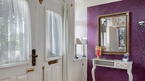 Una habitación con una puerta blanca, una pared morada y un espejo con marco dorado.