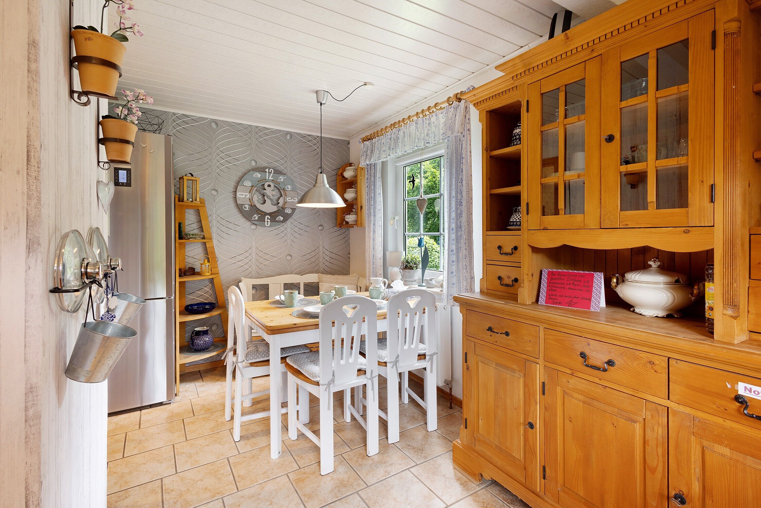 A kitchen with white chairs, a wooden cabinet, and a window with curtains.