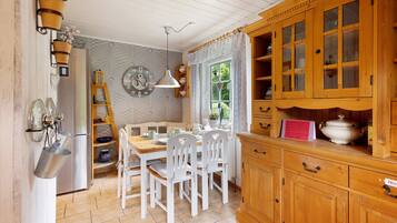 A kitchen with white chairs, a wooden cabinet, and a window with curtains.