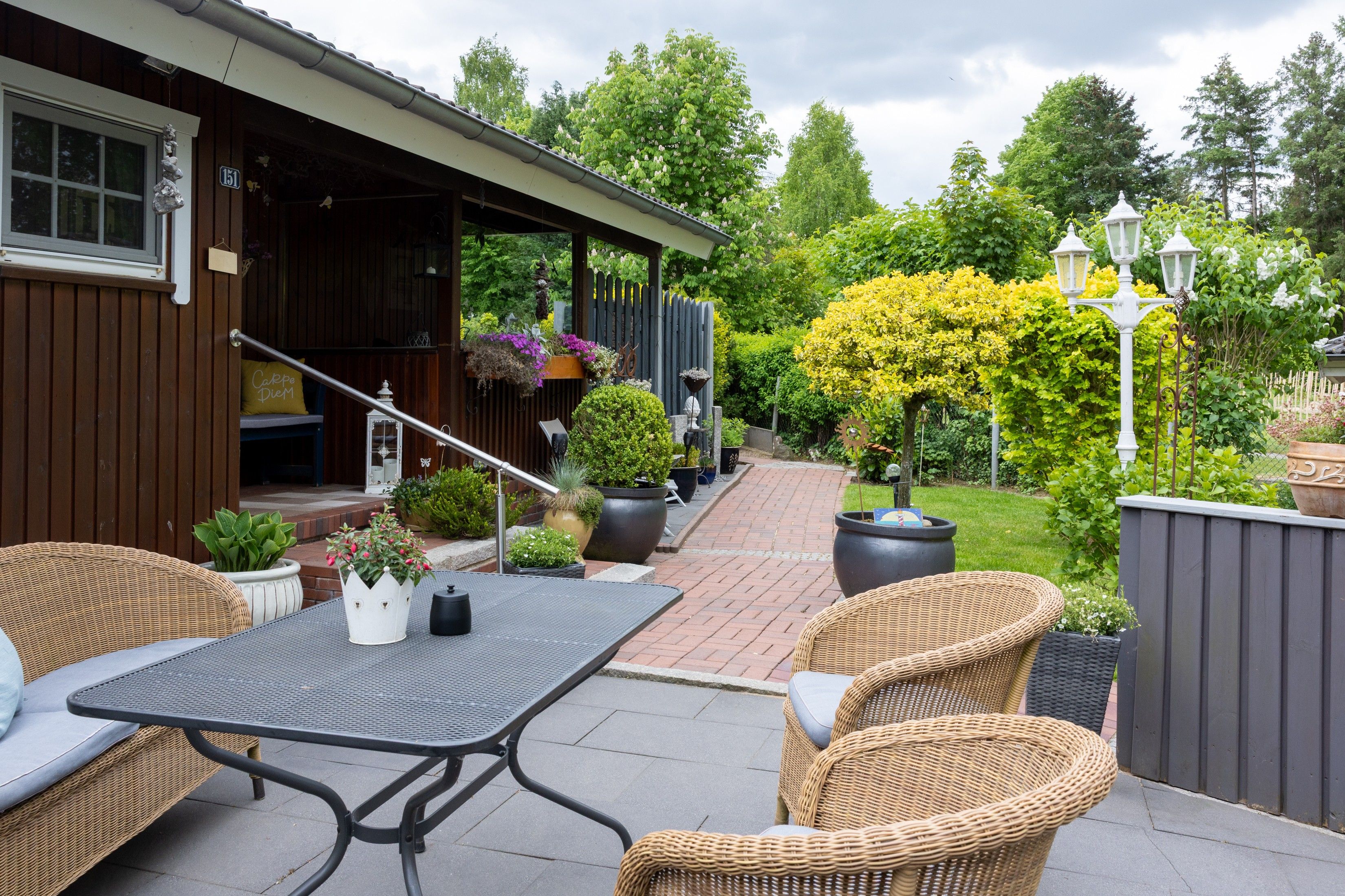 An outdoor patio area with wicker furniture, a covered seating area, and a variety of potted plants.