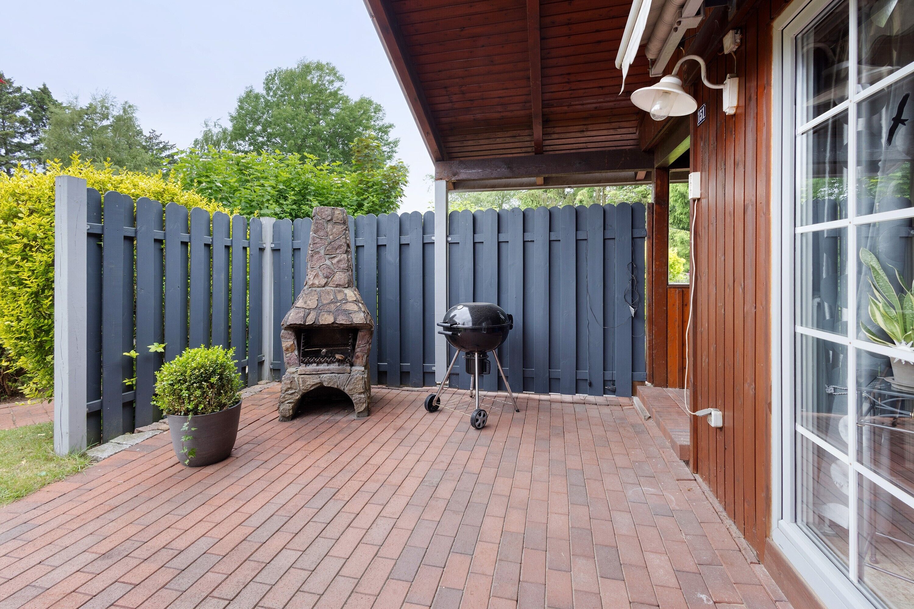 A patio with a brick floor, a stone fireplace, a barbecue grill, and a wooden fence.