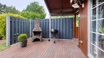 A patio with a brick floor, a stone fireplace, a barbecue grill, and a wooden fence.