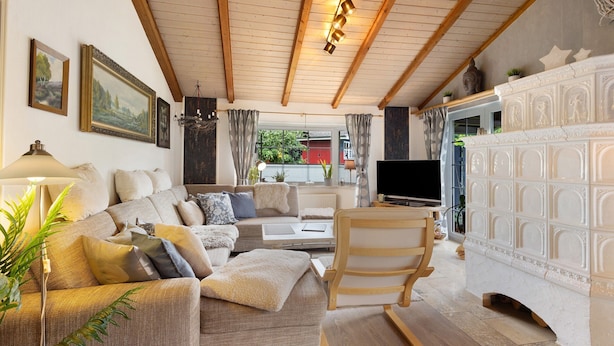 A cozy living room with a sofa, armchair, TV, fireplace, and wooden ceiling beams.