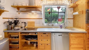A compact kitchen with wooden cabinets, a dishwasher, and a window with a view of greenery.