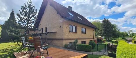 A two-story house with a sloped roof, a brick exterior, and a fenced backyard with a wooden deck and outdoor seating.