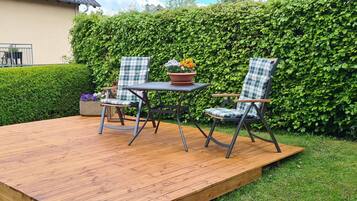 Una terraza de madera con dos sillas y una mesa, rodeada por un seto.