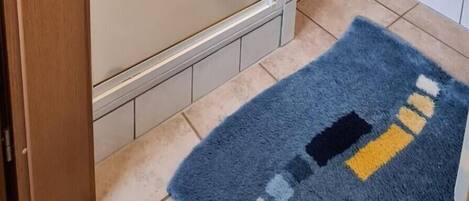A bathroom with a glass shower enclosure, a toilet, and a blue rug with a geometric pattern.