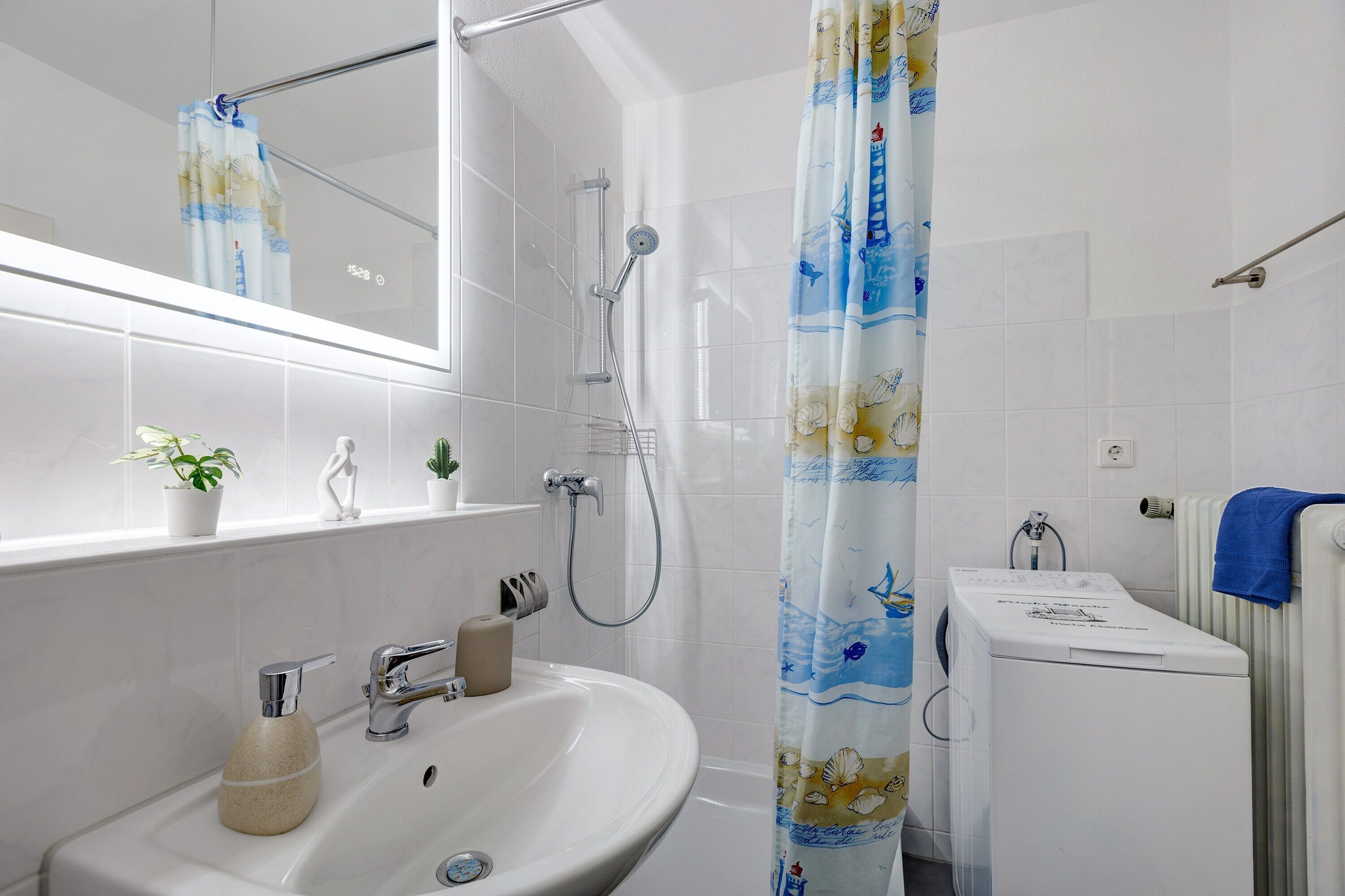 A bathroom with a sink, mirror, shower, and a washing machine.